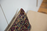 Corner of vintage Kerman rug fragment pillow; intricate ruby, sapphire, and tan curvilinear motifs.