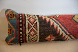 Angled view of a vintage rug pillow showing the coarse pile and geometric motifs on its blue end cap.