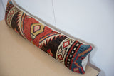 Vintage rug lumbar pillow at an angle, showing its colorful geometric top and solid backing.