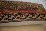 Vintage rug fragment pillow close-up: traditional gold, teal, red ornate border, bottom zipper.