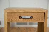 Swappable grey felt handle with leather tabs on a solid oak nightstand drawer.