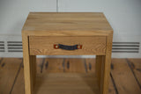 Front view of a wooden nightstand showing its natural oak grain and dark felt handle.