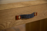 Close-up of the dark grey felt handle with leather tabs and brass rivets on the oak wood drawer.