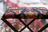 Textured pile of the rug fragment footstool with navy, ruby, and golden geometric patterns.