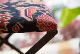 Hand-knotted dark blue, red, cream geometric rug fragment corner on industrial footstool base.