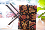 Hand-knotted vintage rug fragment footstool, red and gold patterns on dark ground, industrial base.