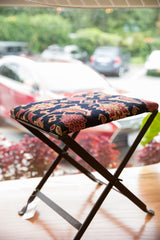 Hand-knotted rug fragment footstool with deep red, gold, and navy botanical pattern.