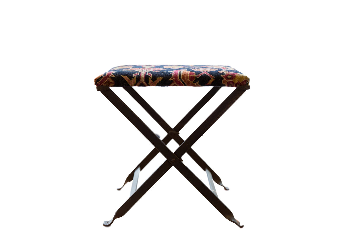 Rug fragment footstool with dark blue, red, yellow patterned vintage seat on folding base.