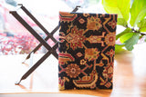 Textured vintage rug fragment footstool with black ground, red, and gold geometric motifs.