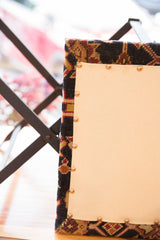 Corner of rug fragment footstool with copper nails, dark blue, red, and gold pattern.