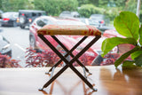 Vintage rug fragment footstool with beige, red, yellow geometric top and dark X-frame base.