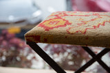 Corner of vintage rug fragment footstool, red and yellow geometric pattern on beige.