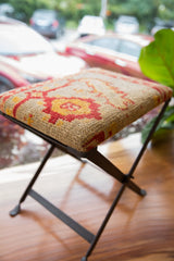 Textural vintage rug fragment footstool with red, yellow, and beige geometric pattern.