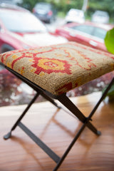 Black metal X-frame base of the vintage rug fragment footstool.