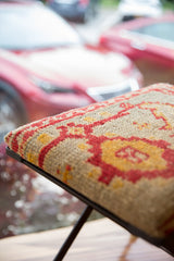 Textured vintage rug fragment on footstool with red and gold geometric motifs.