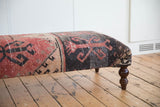 Distressed vintage Oushak rug fragment on ottoman, with faded red, beige, and charcoal patterns.