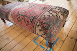 Distressed Oushak rug fragment corner with faded red, charcoal, and beige geometric patterns.