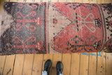 Distressed vintage Oushak fragment featuring faded red, charcoal, and tan geometric patterns.