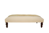 Side view of the canvas ottoman showing its tan rug top and dark turned wood legs.