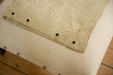 Detail of dark snaps securing a textured vintage rug fragment to the canvas ottoman top.