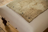 Corner of a textured rug fragment secured with black snaps onto a canvas ottoman.