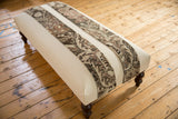Canvas ottoman with two patinated vintage rug fragment strips on dark wooden legs.