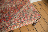 Corner view of vintage Persian rug ottoman, highlighting aged geometric patterns in rusty red and ivory.