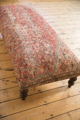 Corner of vintage Persian rug ottoman, with aged red, ivory, blue curvilinear design.