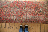 Vintage Persian rug ottoman's top surface, displaying worn traditional patterns in rusty red, ivory, and denim blue.