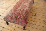 Detail of a dark brown curved wooden leg on the vintage rug ottoman.