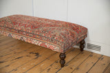 Curved dark wooden leg and rug fragment corner with time-softened red and ivory pattern.