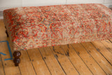 Detail view of vintage Persian rug ottoman's surface, highlighting intricate patterns and aged texture.