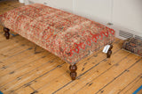 Geometric border design in rusty red, denim blue, and ivory on vintage rug ottoman side.