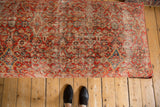Vintage Persian rug ottoman surface with distressed rusty red, tangerine, and ivory patterns.