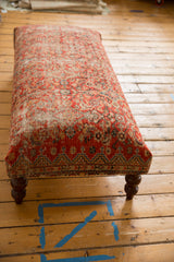 Brass studs accenting the vintage Persian rug ottoman's base and a carved wooden leg.