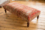 Vintage Persian rug fragment on ottoman corner with geometric border and turned wooden leg.