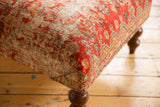 Upholstered corner of a vintage Persian rug ottoman, showing distressed red, ivory, and blue motifs.