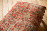 Angled close-up of the ottoman's vintage Persian rug fragment, revealing worn red, orange, and blue motifs.