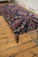 Vintage Yezd rug ottoman corner, navy, faded magenta, ivory floral motifs, turned wood leg.