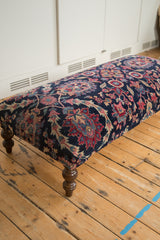 Close-up of early 20th century Yezd rug ottoman, showing navy floral pattern and turned leg.
