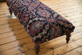 Ornate curvilinear floral pattern on vintage Persian rug ottoman in navy and faded magenta.