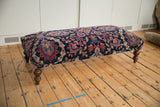 Detail of a curved wooden leg and lower edge of the vintage rug ottoman.