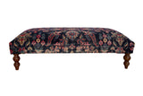 Vintage Persian rug ottoman with a navy floral pattern, magenta accents, and turned wooden legs.