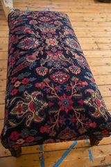 Perspective view of a vintage rug ottoman's rich navy and magenta Persian floral pattern.