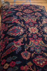 Detailed floral patterns in magenta and indigo blue on the plush, navy wool pile of a vintage Persian rug ottoman.