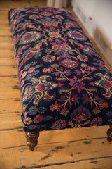 Angled view of a vintage Persian rug ottoman highlighting the floral pattern and a dark curved leg.