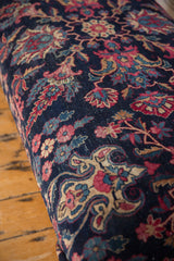 Vintage Persian rug's navy and magenta floral pattern wraps around the ottoman's cushioned edge.