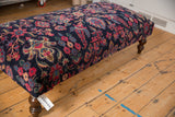 Angled profile of an ottoman with vintage Persian Yezd rug upholstery and curved wood legs.