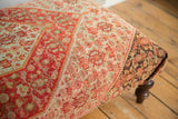 Intricate vintage Persian Senneh rug fragment on ottoman, featuring red-orange, muted blue, and brown patterns.