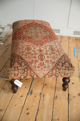 Ottoman's dark carved wooden leg, featuring lower edge of vintage Persian Senneh rug.